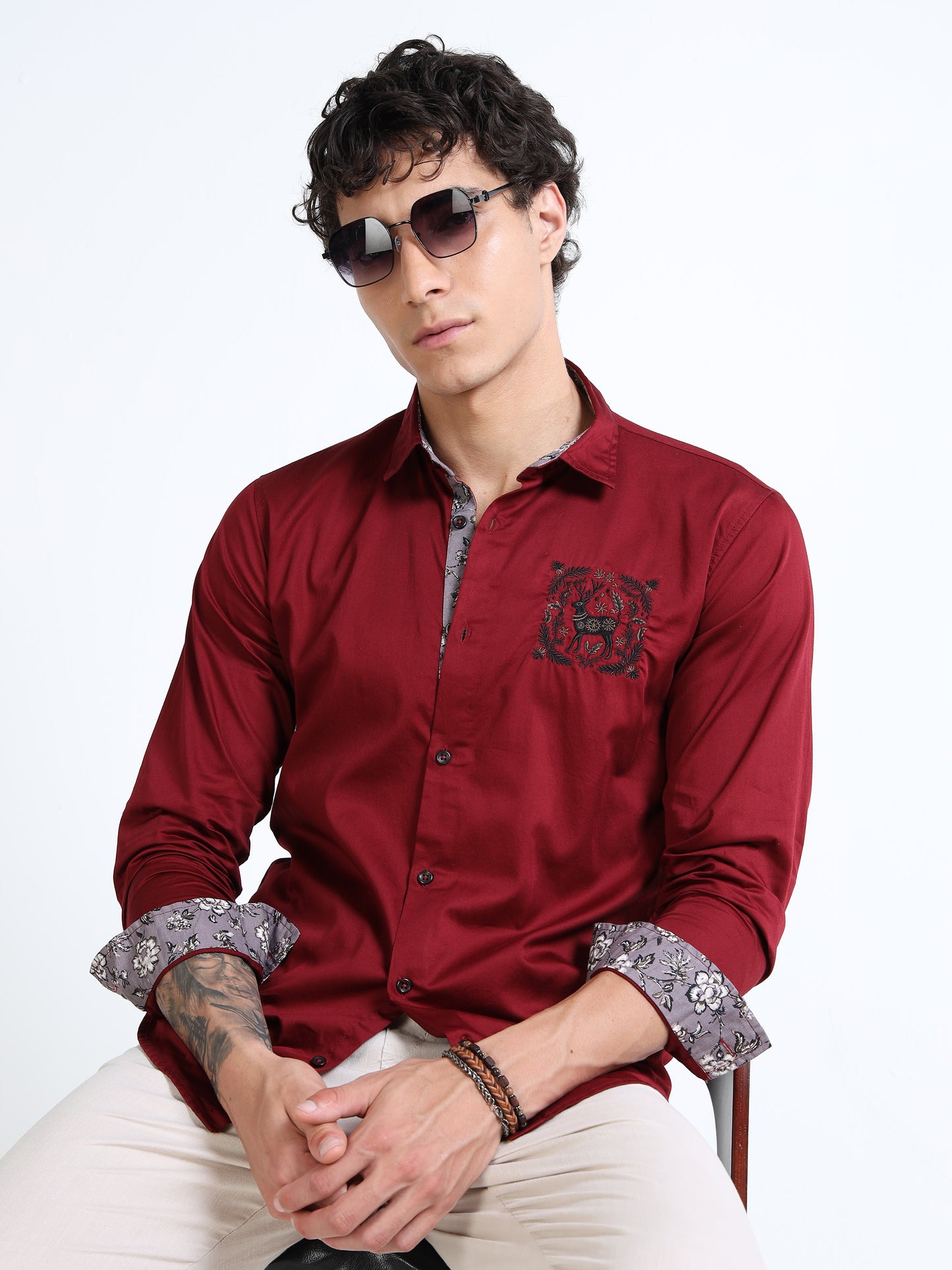 Man wearing a red shirt with floral cuffs and sunglasses on a white background
