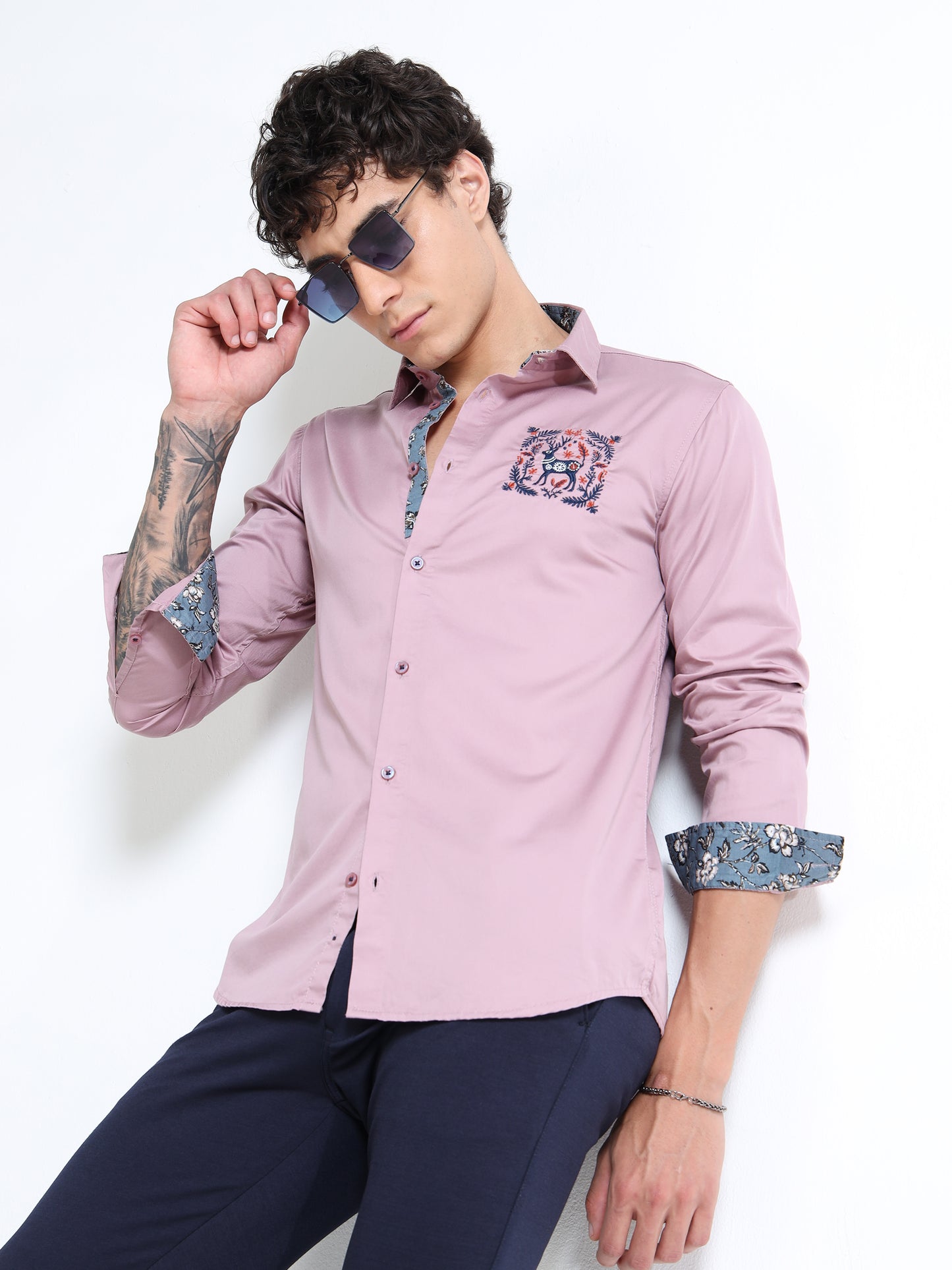Man wearing a pink shirt with floral cuffs and collar, posing against a white background