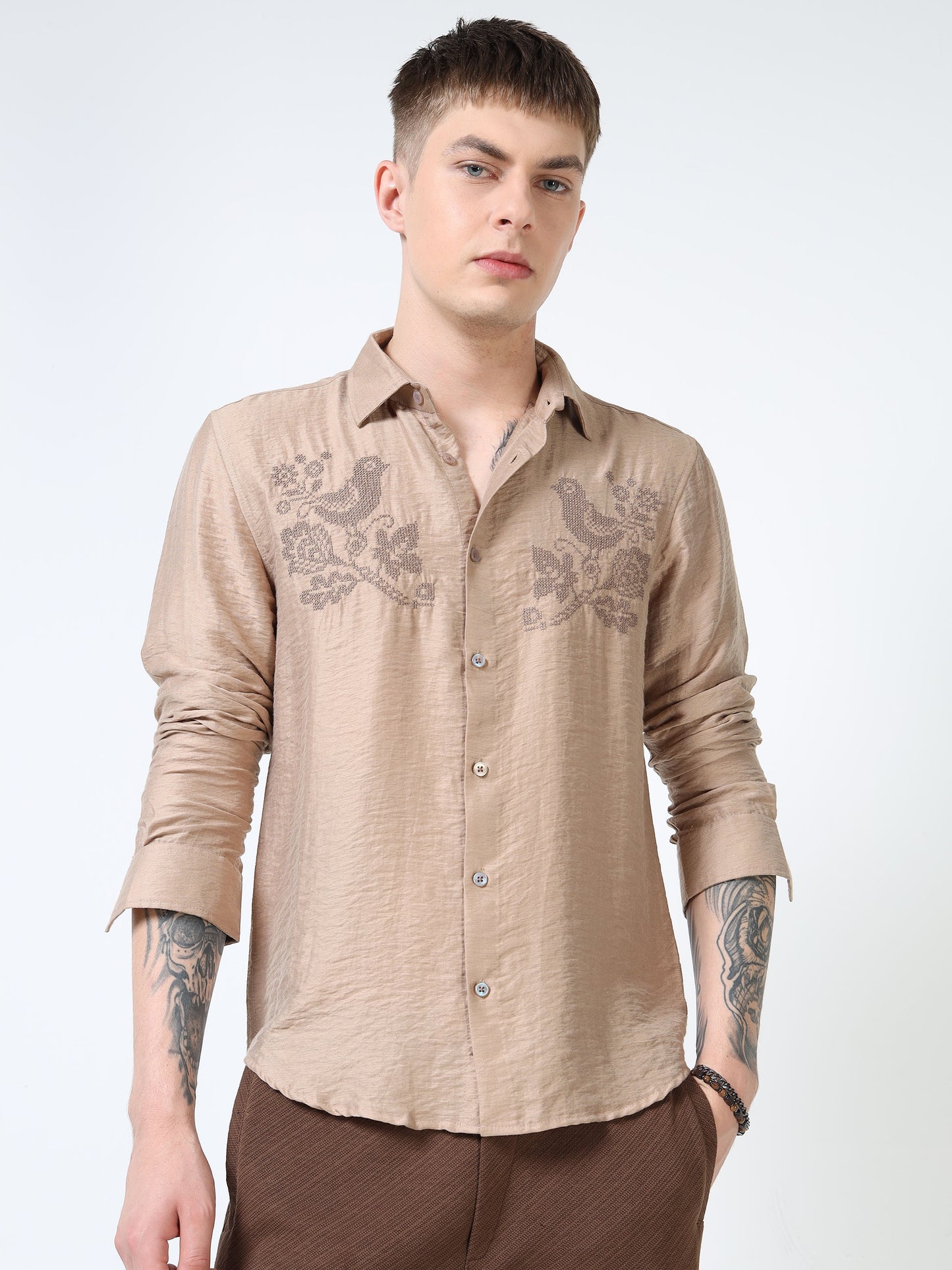 Man wearing a beige embroidered shirt on a white background