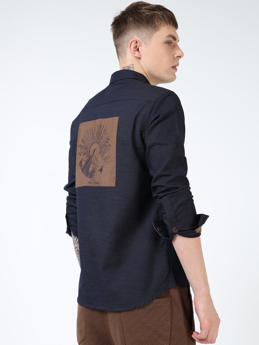 Man wearing a dark blue shirt with a brown patch on the back against a white background