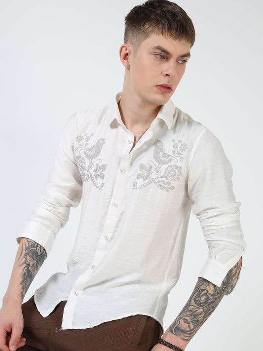 Man wearing a white embroidered shirt on a plain background