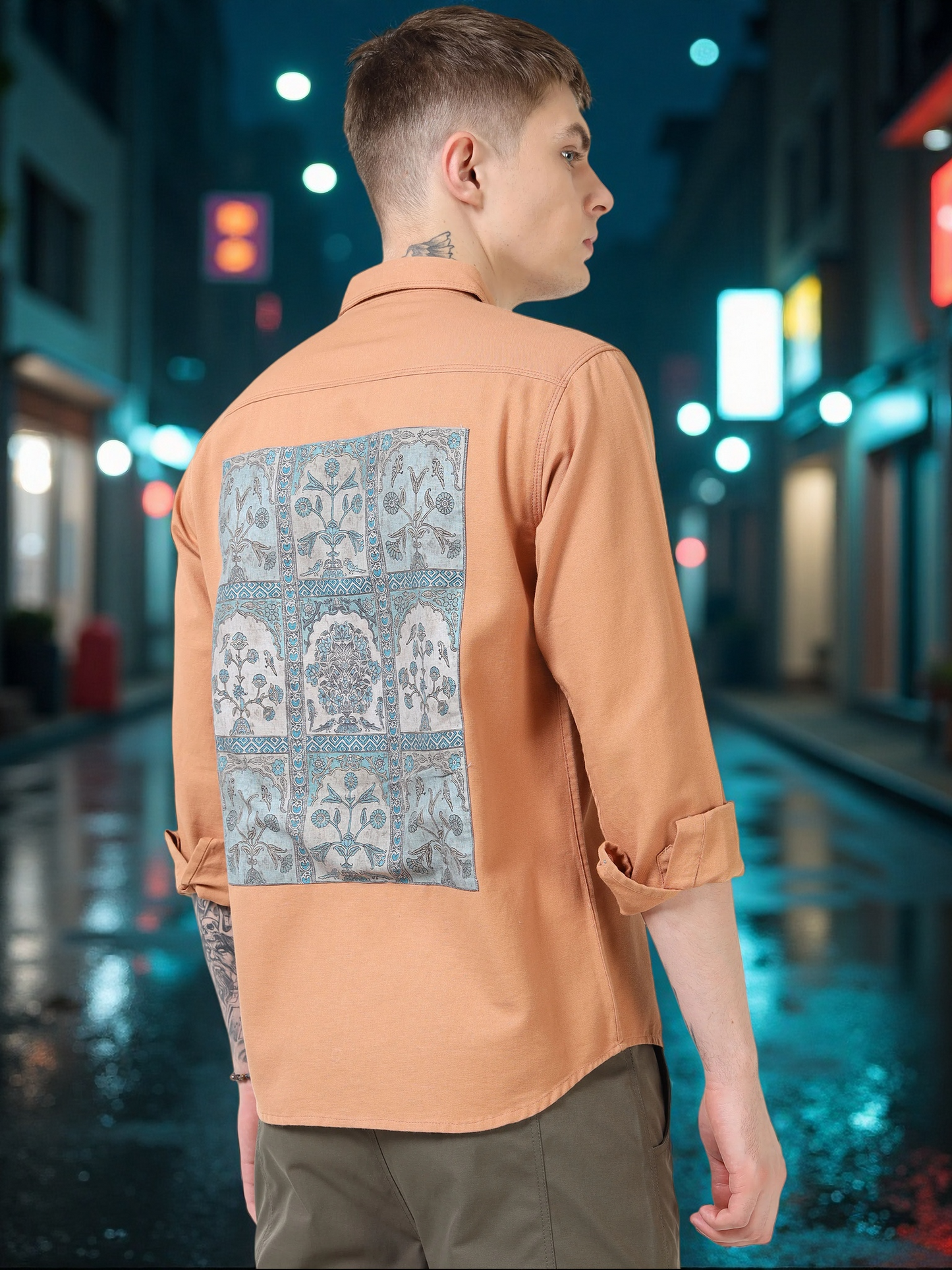 Person wearing a peach-colored shirt with a patterned back panel on a city street at night.